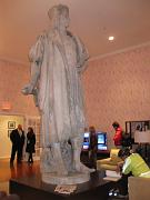  A Coffe talbe (where Columbus is standing onto), a book shelf, a display screen, a couch and several charis are in this modern Living room.